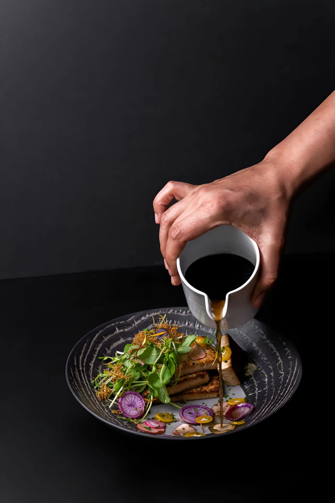 Chef terminando un plato con una salsa en una cocina en penumbra